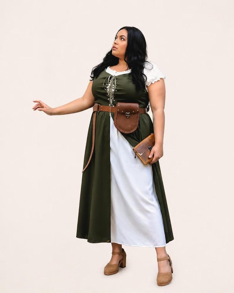 A plus-size model wearing a green and white medieval dress with a brown leather belt bag.