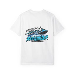Könnte beinhalten: Ein weißes Kurzarm-T-Shirt mit einer Grafik auf der Rückseite, die einen blauen Jetski zeigt, der durch das Wasser fährt. Der Text lautet BAD DAY TO BE A REV LIMITER in Schwarz und Blau, mit SOUTHERN WAKE CO. in kleinerem schwarzem Text darunter.