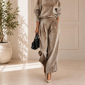 May include: A taupe velvet two-piece set consisting of a long-sleeve mock neck top and wide-leg trousers with front pleats. The outfit is paired with a black handbag and pointed-toe heels. The Willson Boutique logo is visible in the top right corner.