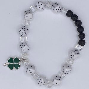 Pode incluir: Uma pulseira de contas com dados brancos de pontos pretos, espaçadores de cristal transparente facetado e uma secção de contas de lava preta porosa. Um pendente de metal prateado em forma de trevo de quatro folhas com esmalte verde pendurado.