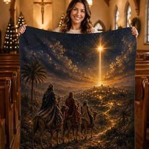 May include: A rectangular throw blanket featuring a detailed illustration of the three wise men riding camels toward a glowing star above a distant city. The scene includes a dark night sky, palm trees, and a path leading to the illuminated town.