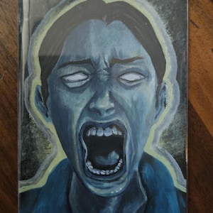 Può includere: Una stampa artistica rettangolare che raffigura il ritratto dai toni blu di una persona con la bocca spalancata e occhi bianchi luminosi. La figura è circondata da un tenue contorno giallo su uno sfondo scuro, creando un effetto di contrasto.