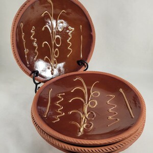 May include: Three brown terracotta plates with a decorative design of a stylized plant with yellow glaze. The plates are stacked on top of each other.
