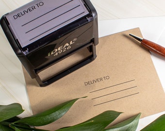 May include: A black self-inking stamp with the text "DELIVER TO" and three lines for writing. The stamp is on a brown envelope with the same text and lines. A brown pen is on the envelope.