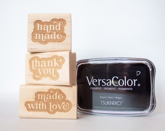 Pode incluir: Três carimbos de madeira com as palavras "hand made", "thank you" e "made with love" empilhados um em cima do outro. Um almofada de tinta preta com a etiqueta "VersaColor" está ao lado dos carimbos.