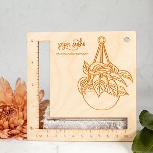 May include: A wooden ruler with a hanging plant design and the text "paper sushi PAPERSUSHISHOP.COM". The ruler has inch and centimetre markings.