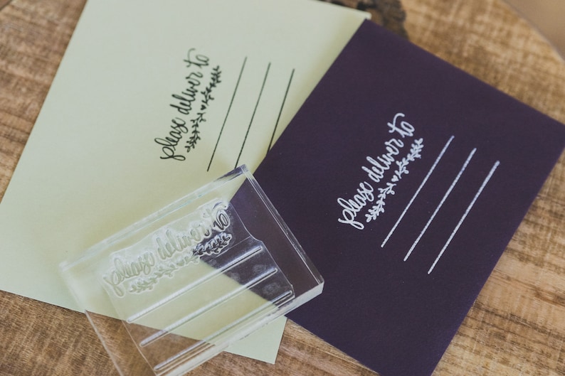 May include: A clear acrylic stamp with the text "Please deliver to" and a small floral design. The stamp is on top of a purple envelope with the same text and design stamped in white.