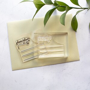 May include: Clear acrylic stamp set with two stamps. The first stamp says "please deliver to" with a small arrow pointing to the right. The second stamp says "please deliver to" with a decorative flourish.