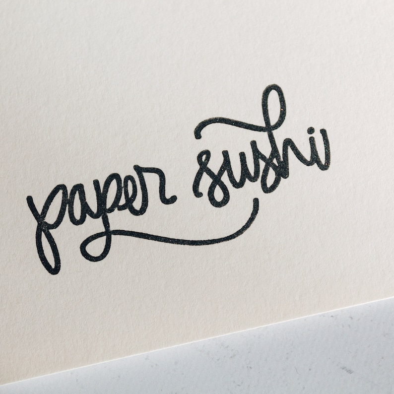 May include: Handwritten calligraphy on a white background that says "paper sushi".