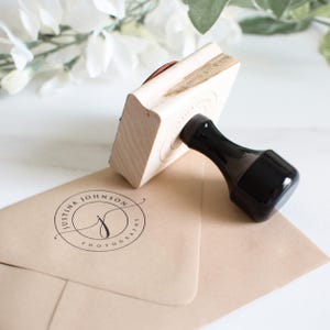 May include: A wooden stamp with a black handle. The stamp is used to create a circular logo with the text "Justina Johnson Photography" and a stylised letter "J".