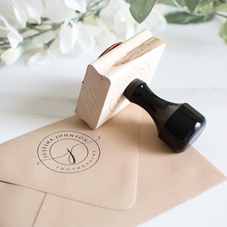 May include: A wooden stamp with a black handle. The stamp is used to create a circular logo with the text "Justina Johnson Photography" and a stylised letter "J".