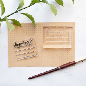 May include: Two clear acrylic stamps on a brown background. The first stamp says "Please deliver to" with a small floral design. The second stamp has three blank lines.