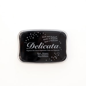 May include: A black ink pad with the text "Delicata" in a silver script font. The ink pad is labeled "Rich and Radiant" and "Black Shimmer".