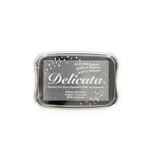 May include: A black ink pad with the text "Delicata" in white. The ink pad is labeled "Rich and Radiant, Riche et Radiant, Rico y Radiante". The ink pad is also labeled "Silvery Shimmer, Argent Chatoyant, Brillo Plateado".