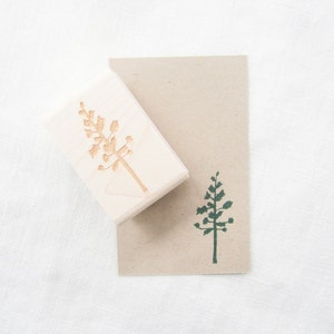 May include: A wooden stamp with a carved image of a tree. The stamp is on top of a brown card with a green ink impression of the tree.