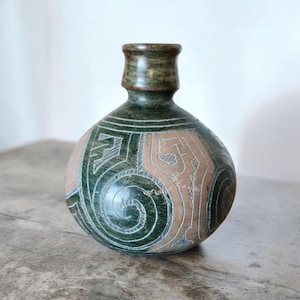 Peut inclure: Un vase rond et bulbeux avec un col étroit et un bord évasé. La surface présente un design bicolore avec des sections vert foncé et beige clair, orné de motifs géométriques et en spirale complexes gravés à la main dans la matière.