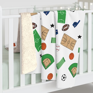 May include: A white sherpa-lined blanket featuring a repeating pattern of various sports equipment and pitches, including basketball courts, baseball diamonds, football pitches, American footballs, basketballs, footballs, baseballs, and black stars.