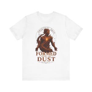 May include: A white short-sleeved t-shirt featuring a brown graphic print of a figure emerging from dust. The text reads ORIGINAL SKIN, FORMED FROM THE DUST, and GENESIS 2:7. The figure has a glowing light at the center of the chest area.