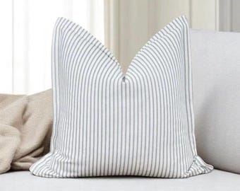 May include: A white pillow with thin blue stripes. The pillow is on a light gray couch.