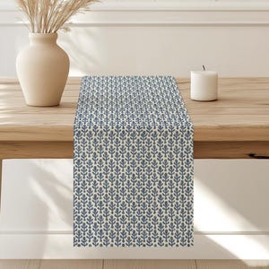 May include: A blue and white patterned table runner with a floral design. The runner is on a wooden table with a vase of dried grass.