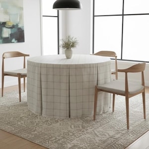 May include: A round dining table with a plaid tablecloth and three wooden chairs. The table is covered with a light-colored fabric with a plaid pattern. The chairs have light-colored seats and curved wooden backs. A patterned rug is beneath the table.