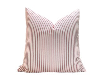 May include: A white pillow with thin red stripes. The pillow is made of a soft, woven fabric.