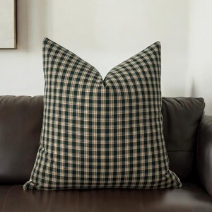 May include: A green and cream plaid throw pillow with a square pattern. The pillow is sitting on a brown leather couch.