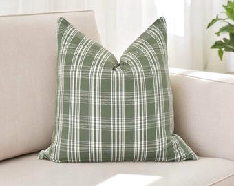 May include: A green and white plaid throw pillow with a soft, textured fabric. The pillow is sitting on a light beige couch.
