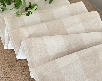 May include: A beige and white checkered table runner made of linen. The runner is folded and laid on a wooden surface. A green plant is in the background.