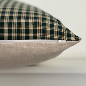 May include: A green and cream plaid pillow with a zipper closure. The pillow is made of a soft, woven fabric.