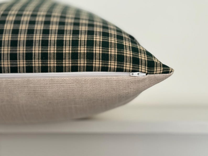 May include: A green and cream plaid pillow with a zipper closure. The pillow is made of a soft, woven fabric.