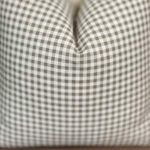 Puede incluir: Un coj&iacute;n cuadrado con un patr&oacute;n cl&aacute;sico de cuadros vichy en color topo y blanco. La tela presenta un dise&ntilde;o de cuadr&iacute;cula repetitivo a peque&ntilde;a escala con una apariencia suave y mullida, creando una hendidura marcada en el centro.