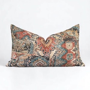 May include: A rectangular decorative pillow with a patterned design. The pillow features a mix of colors, including red, blue, beige, and brown. The pattern appears to be a traditional, possibly tribal, design. The pillow is placed on a white surface.