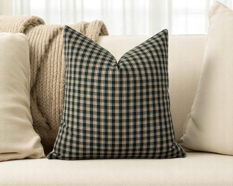 May include: A black and cream plaid throw pillow with a square shape. The pillow is sitting on a white couch.