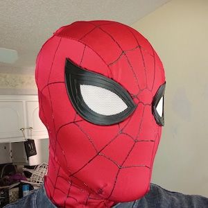 Op de afbeelding: Een rood stoffen masker met een zwart webpatroon over het oppervlak. Het masker bevat twee grote, amandelvormige ooglenzen met zwarte randen en witte mesh-inzetstukken, die het hoofd en de nek volledig bedekken in een nauwsluitend ontwerp.