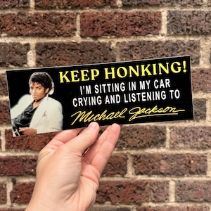 Könnte beinhalten: Ein rechteckiger Aufkleber mit schwarzem Hintergrund und einem Foto von Michael Jackson auf der linken Seite. Der Text lautet KEEP HONKING! I'M SITTING IN MY CAR CRYING AND LISTENING TO Michael Jackson in gelber und weißer Schrift.