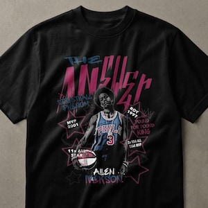 以下が含まれることがあります： 黒いTシャツで、青いフィラデルフィアのジャージを着てバスケットボールを持っているアレン・アイバーソンのグラフィックが描かれています。テキストには、THE ANSWER、STREETBALL PHENOM、ROY 1997、MVP 2001、POUND FOR POUND KING、11x ALL STAR、2x NBA ALL STAR MVP、ALLEN IVERSONが含まれています。
