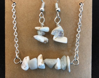 May include: A silver chain necklace with a row of white and grey stones. Matching earrings with white and grey stones hang from silver hooks.