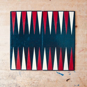 May include: A black, red, and white checkerboard game board with 12 triangles on each side. The board is made of wood and has a smooth surface.