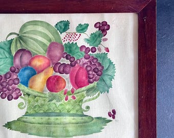 May include: A framed watercolor painting of a fruit bowl filled with watermelon, plums, grapes, peaches, and pears. The bowl is green and has a scalloped edge. The fruit is arranged in a pleasing and symmetrical way. The painting is set against a white background.