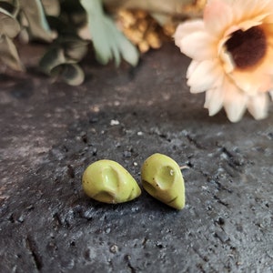 May include: A pair of small, green ceramic earrings in the shape of a teardrop. The earrings are on a dark, textured surface.