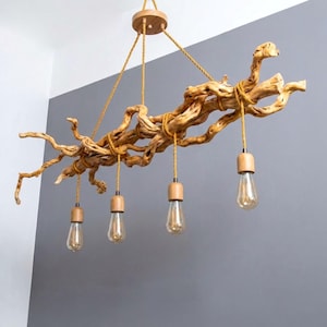 May include: A hanging light fixture featuring a large, natural, light-brown driftwood branch suspended by yellow fabric cords. Four light bulbs with light-wood sockets hang from the branch at varying heights, connected by matching yellow cords.