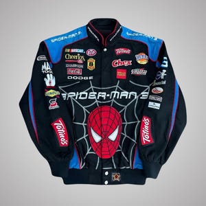 Peut inclure: Une veste de course noire avec des empiècements d'épaules bleus et un grand motif Spider-Man 3 sur le devant. La veste est ornée de divers logos de marques brodés, notamment NASCAR, Cheerios, Coca-Cola, Dodge, Totino's et Wells Fargo.
