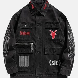 Könnte beinhalten: Eine schwarze Jeansjacke mit rotem Slipknot-Logo und Ziegenemblem auf den Brusttaschen. Die Ärmel haben weiße Tribal-Grafiken, während der untere Vorderbereich einen Barcode und den Schriftzug (sic) zeigt. Roter Text ist auf dem Kragen gestickt.