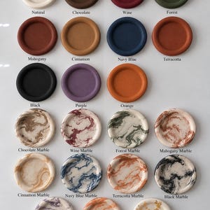 May include: A collection of round, shallow trays arranged in rows. The top three rows feature solid colors including natural, chocolate, wine, forest, mahogany, cinnamon, navy blue, terracotta, black, purple, and orange. The bottom rows show marble patterns and a natural gold flake finish, each labeled with its corresponding color name.