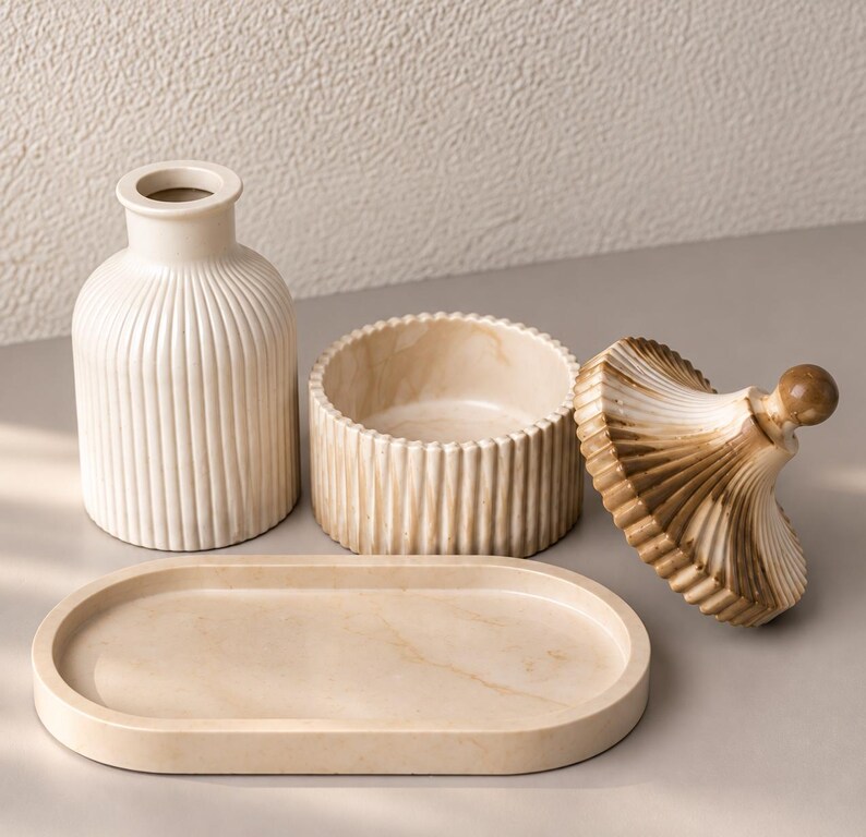May include: A set of cream-colored home decor items including a ribbed vase, a round lidded container with a marbled finish, and an oval tray. The lid of the container is detached, showing a brown and cream marbled pattern with a small knob handle.
