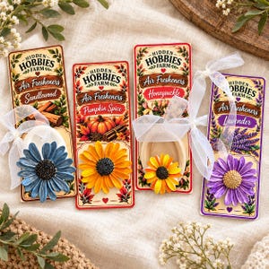 May include: Four Hidden Hobbies Farm air fresheners on rectangular cardboard backing cards. Each features a different flower-shaped ornament in blue, yellow, orange, or purple, tied with a white sheer ribbon and labeled Sandlewood, Pumpkin Spice, Honeysuckle, or Lavender.