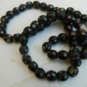 May include: A dark beaded necklace with oval beads. Each black bead features colourful accents, including pink, blue, and yellow dots. The necklace is displayed on a white surface.