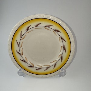 May include: A round ceramic plate with an off-white center and a wide, golden-yellow border. The border features a delicate, hand-painted wreath of brown leaves. The rim of the plate has a raised, textured rope-like pattern around the edge.