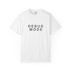 Peut inclure: Un t-shirt blanc à manches courtes et col rond avec le texte DEBUG MODE imprimé en lettres capitales noires au centre de la poitrine. Le vêtement présente une coupe standard avec un col côtelé et une étiquette de marque visible à l'intérieur.